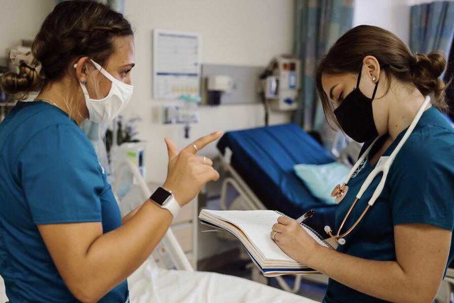 two nursing students talking while one student takes notes in a notebook